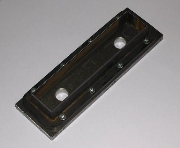 Voorbeeld van stansmes te plaatsen in een pers met parallelle platen, met metalen basisplaat en 2 openingen om het uitgesneden proefexemplaar uit te werpen.